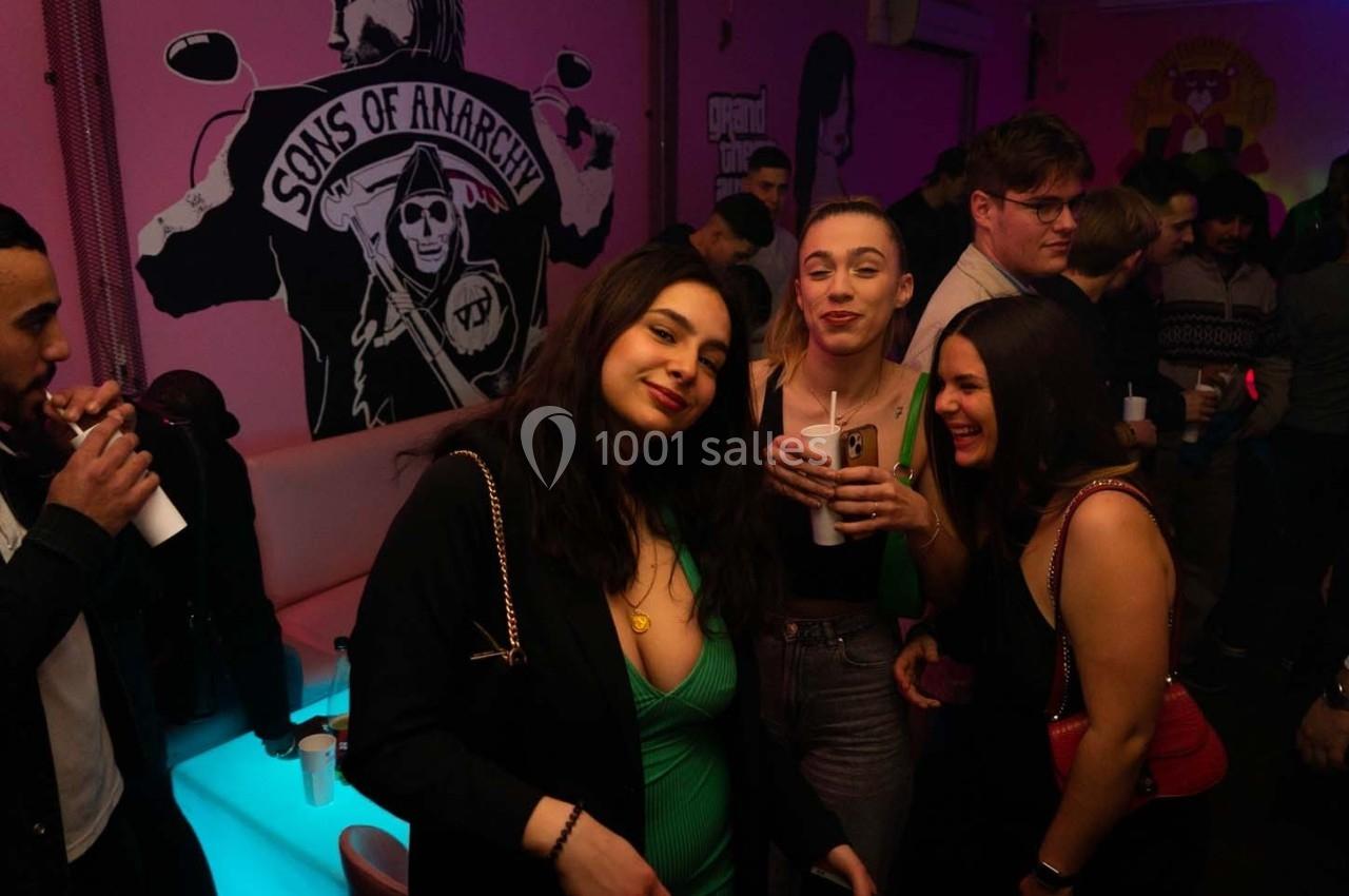 Des personnes discutent et boivent dans un bar à l'ambiance colorée avec une fresque murale en arrière-plan.