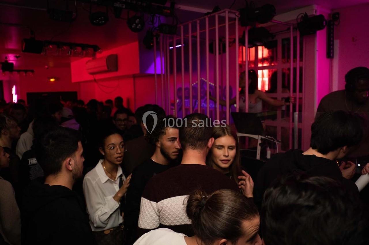 Groupe de personnes discutant dans une ambiance de soirée avec éclairage tamisé et néons roses.