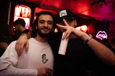 Salle de bar aux murs roses avec banquettes blanches, tabourets assortis et néons décoratifs.