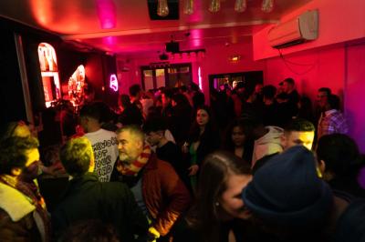 Salle de bar aux murs roses avec banquettes blanches, tabourets assortis et néons décoratifs.
