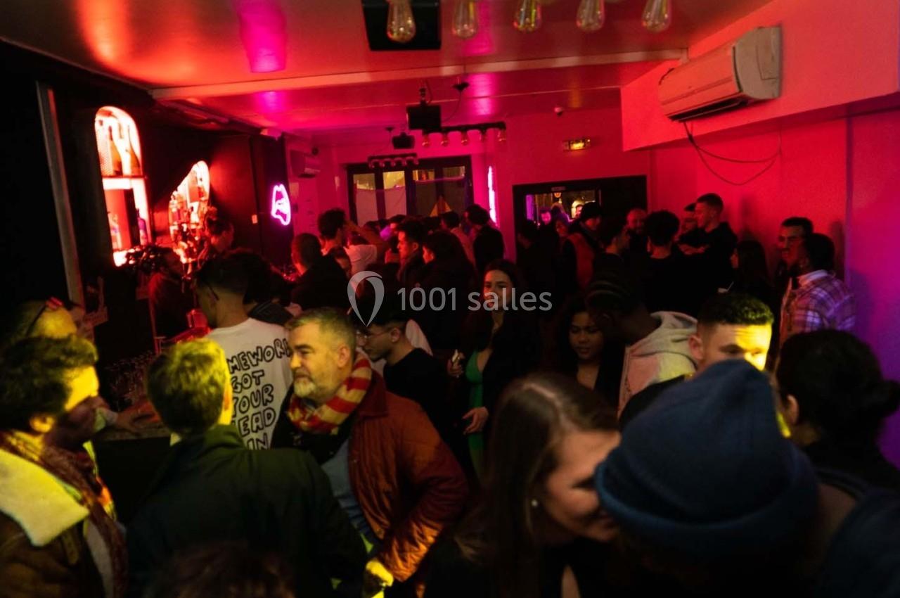 Personnes rassemblées dans un bar ou club, éclairé par des lumières colorées, discutant et profitant de l'ambiance.