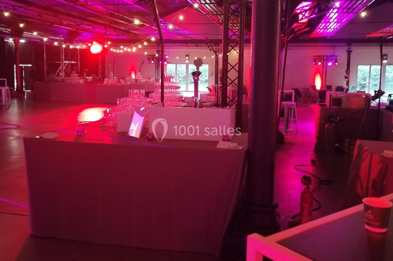 Salle de réception avec éclairage rouge, tables dressées et équipements techniques en arrière-plan.