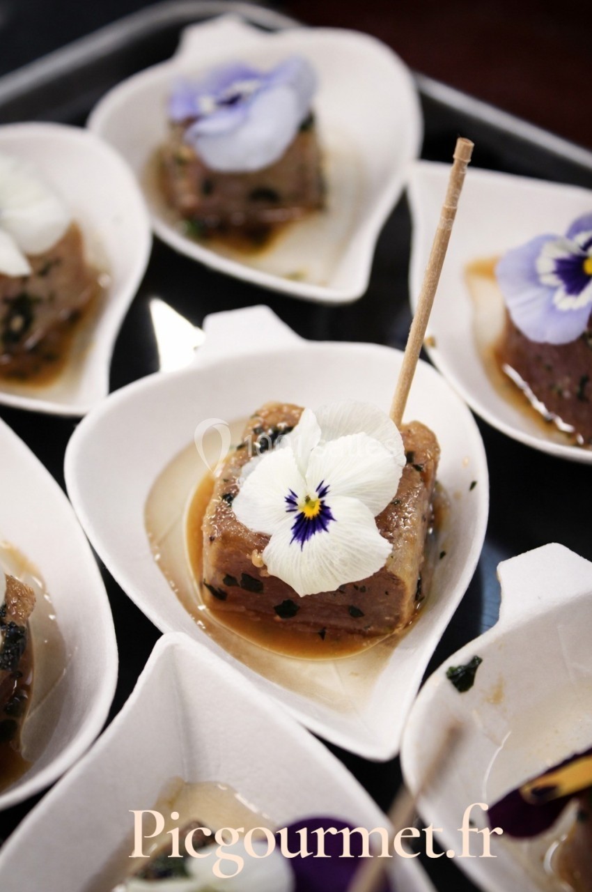 Cube de tartare de poisson garni d'une fleur comestible, présenté dans une coupelle individuelle en forme de cœur.
