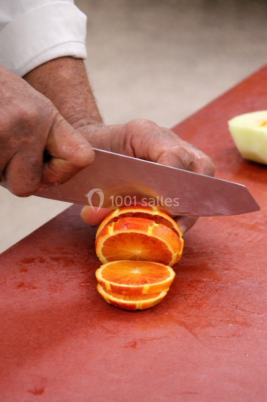 Un homme tranche une orange sanguine sur une planche rouge avec un couteau.