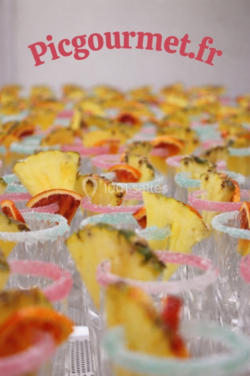 Verres décorés de tranches d'ananas et d'agrumes, bordés de sucre coloré, alignés sur une table.