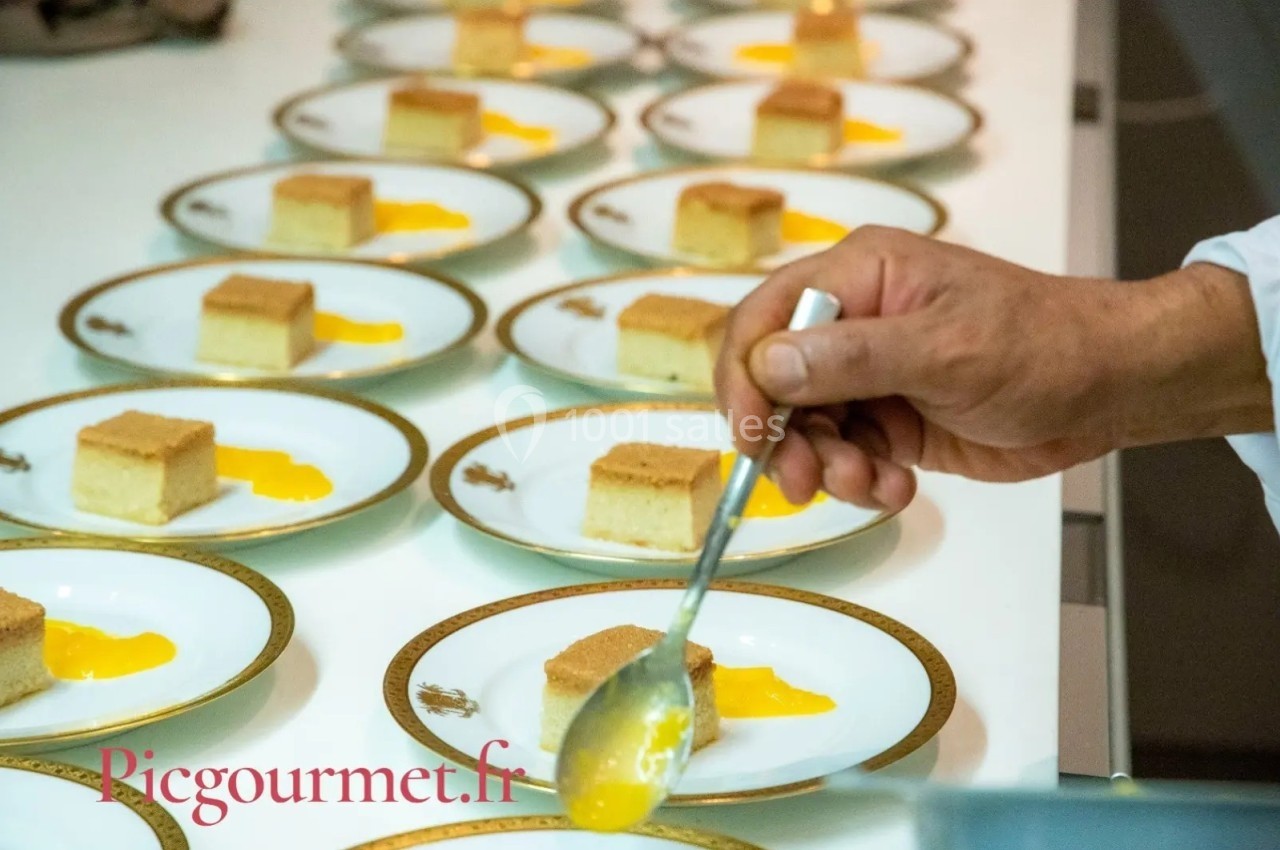 Un chef dépose une sauce jaune sur des assiettes contenant des portions de gâteau rectangulaires.