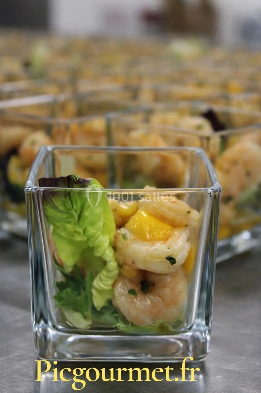Verrine contenant des crevettes, morceaux de mangue et salade verte, présentée sur une table avec d'autres verrines.