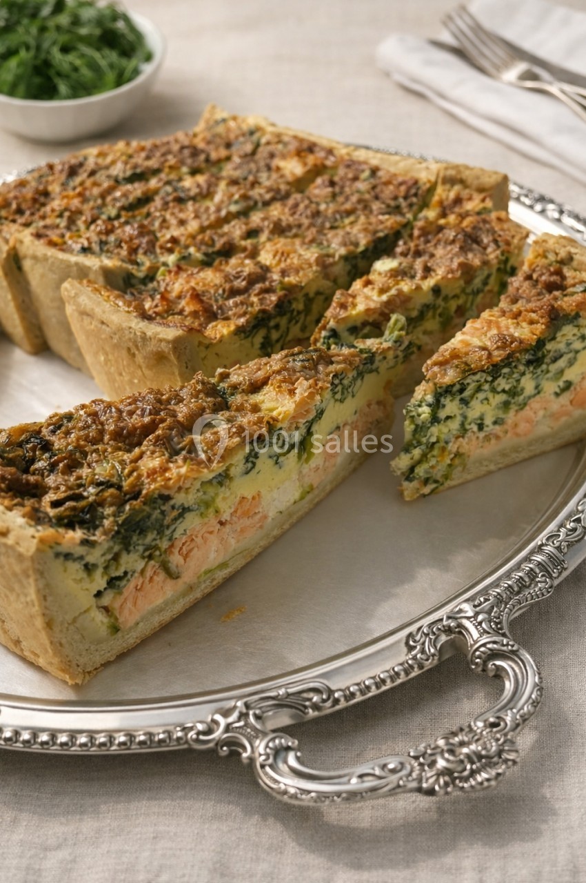 Quiche aux épinards, saumon et fromage, servie sur un plateau en métal argenté avec des parts découpées.