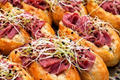 Petits pains garnis de pastrami, germes de luzerne et graines noires, disposés sur un plateau en métal.