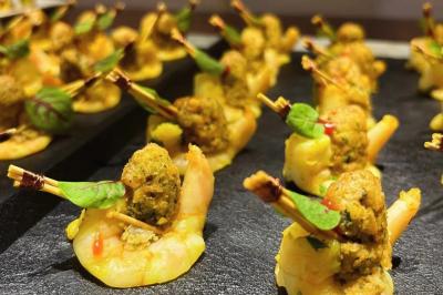 Crevettes garnies de boulettes épicées et décorées de feuilles vertes, présentées sur un plateau noir.