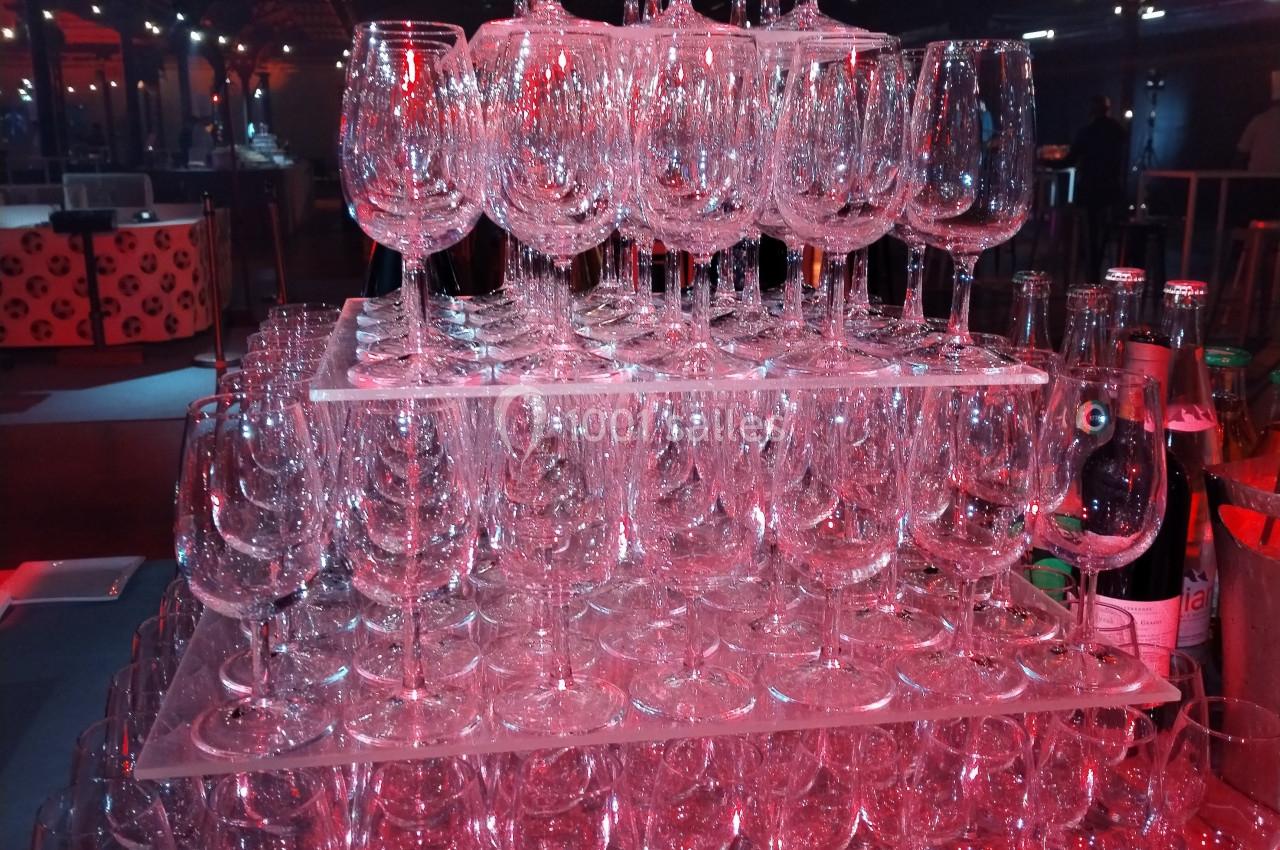 Empilement de verres à pied transparents sur plusieurs niveaux, éclairés par une lumière rouge dans un espace intérieur.