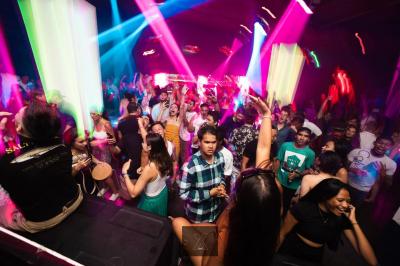 Salle de discothèque avec éclairage coloré, colonnes lumineuses et bar en arrière-plan.