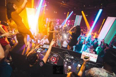 Salle de discothèque avec éclairage coloré, colonnes lumineuses et bar en arrière-plan.