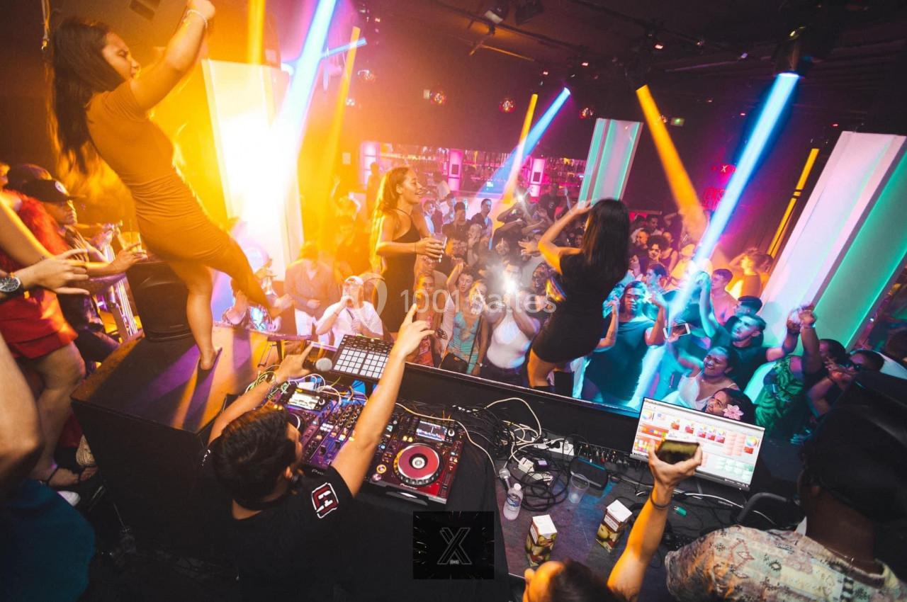 Des personnes dansent et s'amusent dans une boîte de nuit animée avec lumières colorées et DJ sur scène.