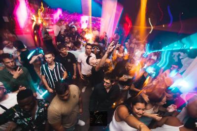 Salle de discothèque avec éclairage coloré, colonnes lumineuses et bar en arrière-plan.