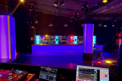 Salle de discothèque avec éclairage coloré, colonnes lumineuses et bar en arrière-plan.