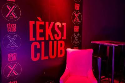 Salle de discothèque avec éclairage coloré, colonnes lumineuses et bar en arrière-plan.