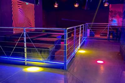 Salle de discothèque avec éclairage coloré, colonnes lumineuses et bar en arrière-plan.