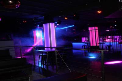 Salle de discothèque avec éclairage coloré, colonnes lumineuses et bar en arrière-plan.