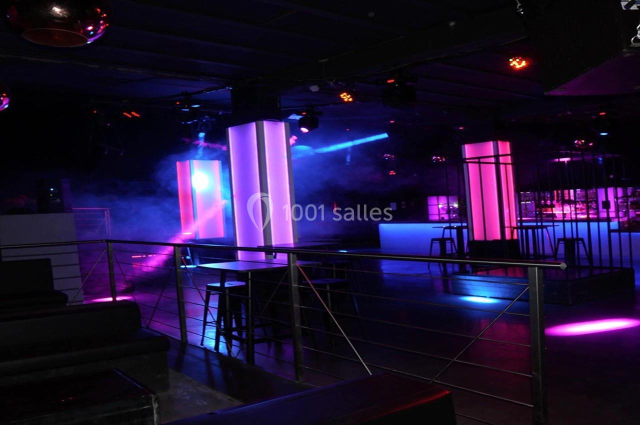 Salle de discothèque avec éclairage coloré, colonnes lumineuses et bar en arrière-plan.