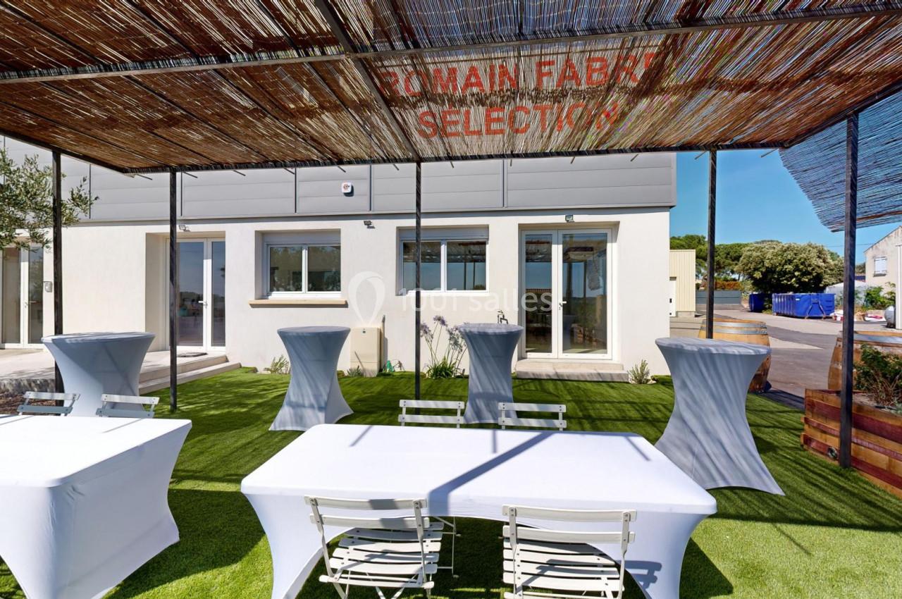 Terrasse extérieure avec tables et chaises blanches sur gazon artificiel, ombragée par une pergola en canisses.