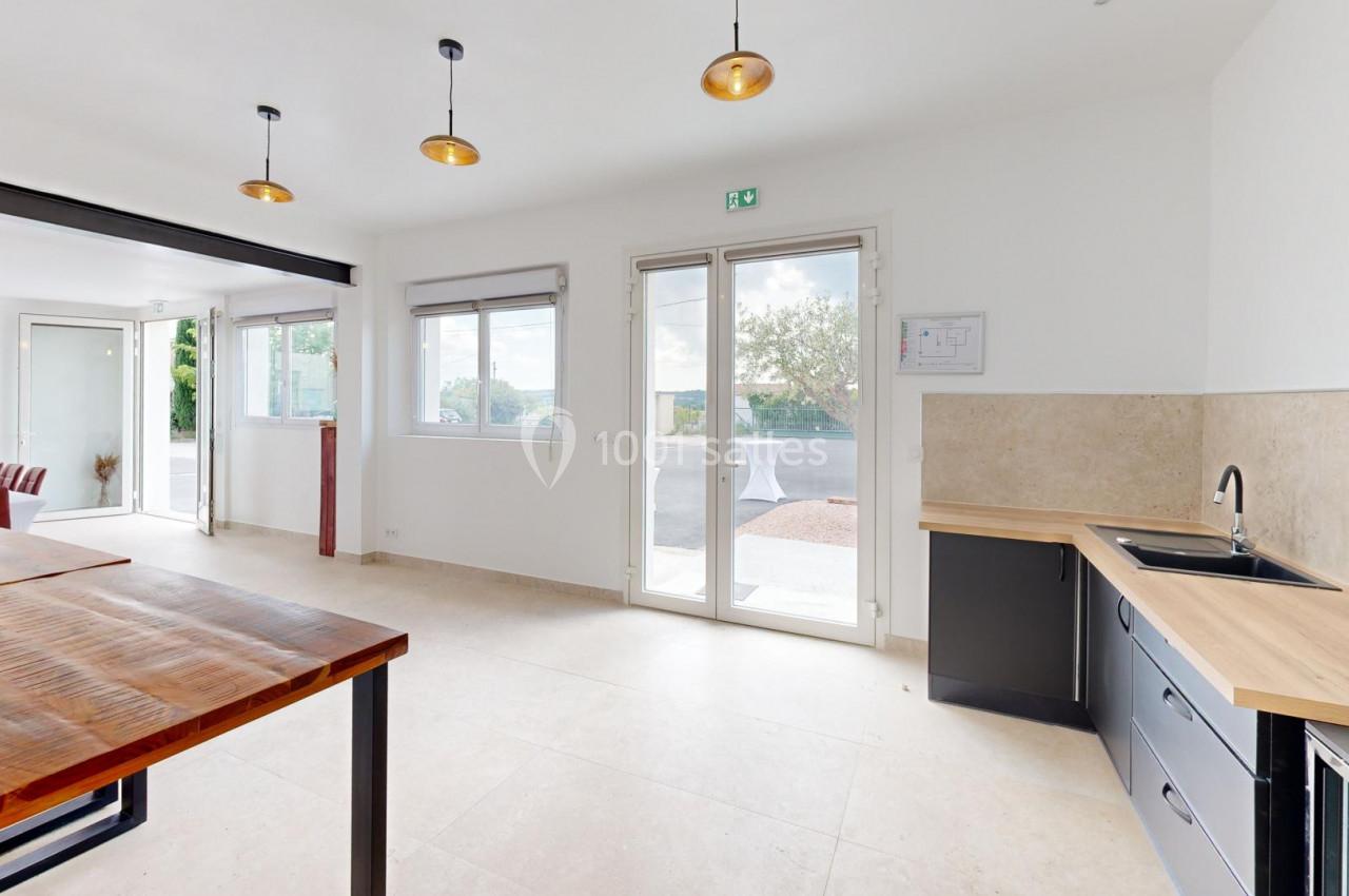 Cuisine ouverte lumineuse avec plan de travail en bois, évier intégré, grandes fenêtres et suspension moderne.