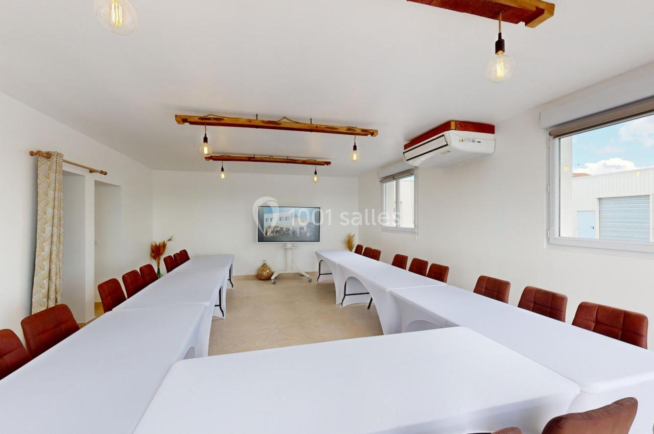 Salle de réunion lumineuse avec deux grandes tables en U, chaises marron, décor minimaliste et fenêtres donnant sur l…