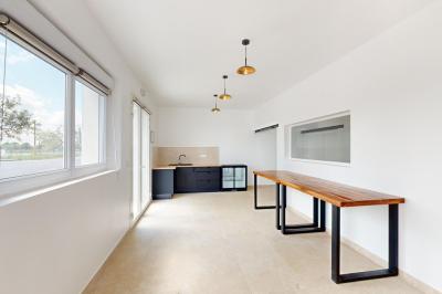 Salle de bain avec murs en carrelage beige, lavabo mural avec accessoires et toilettes séparées par une cloison.