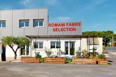 Salle de bain avec murs en carrelage beige, lavabo mural avec accessoires et toilettes séparées par une cloison.