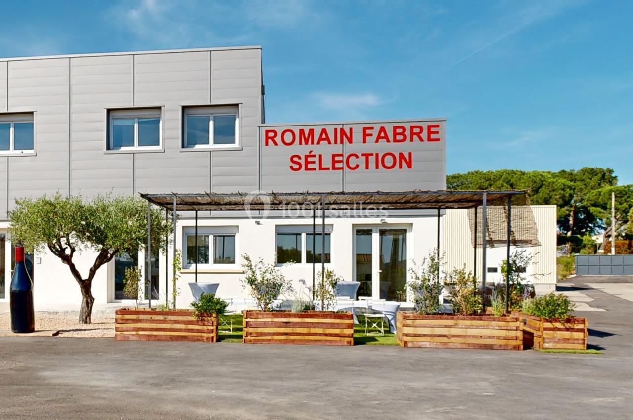 Façade d'un bâtiment moderne avec enseigne ’Romain Fabre Sélection’, terrasse aménagée et jardinières en bois.