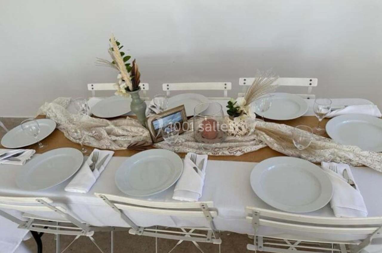 Table dressée avec une nappe blanche, vaisselle simple, décorations naturelles et un cadre photo au centre.