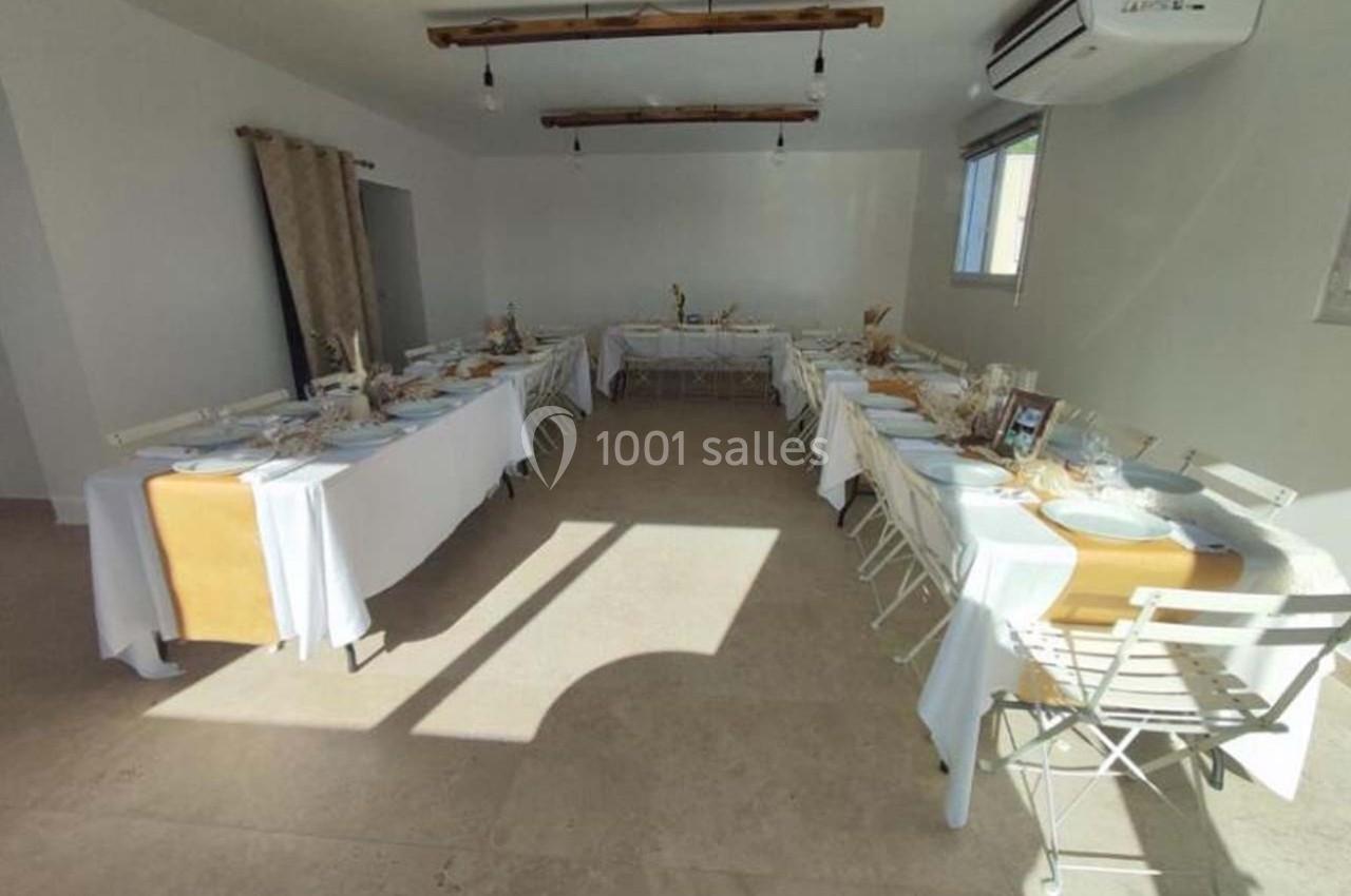 Salle lumineuse aménagée avec des tables dressées pour un repas, disposées en U, dans un décor sobre et moderne.