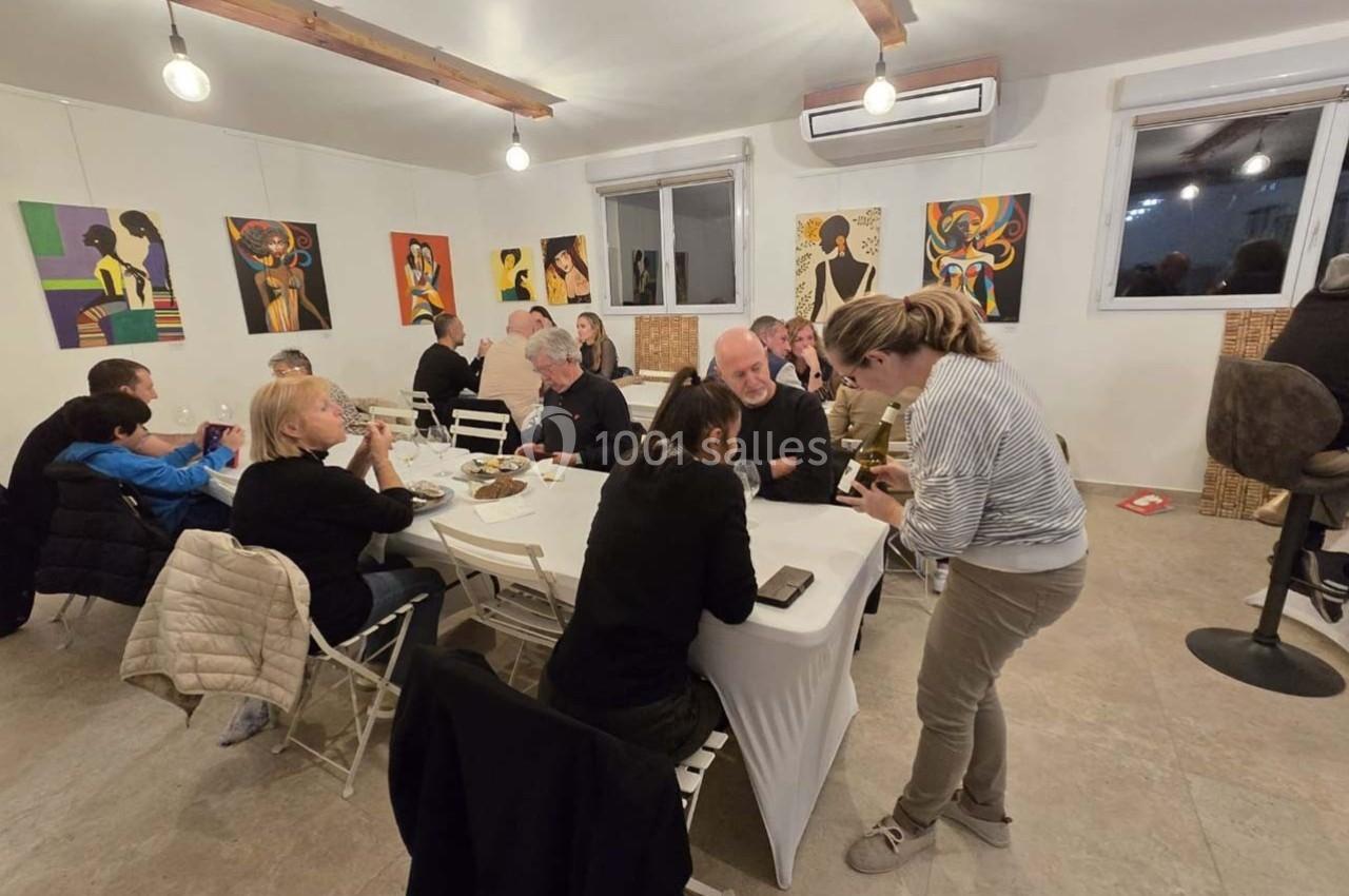 Des personnes discutent et partagent un repas autour d'une grande table dans une salle décorée de tableaux colorés.
