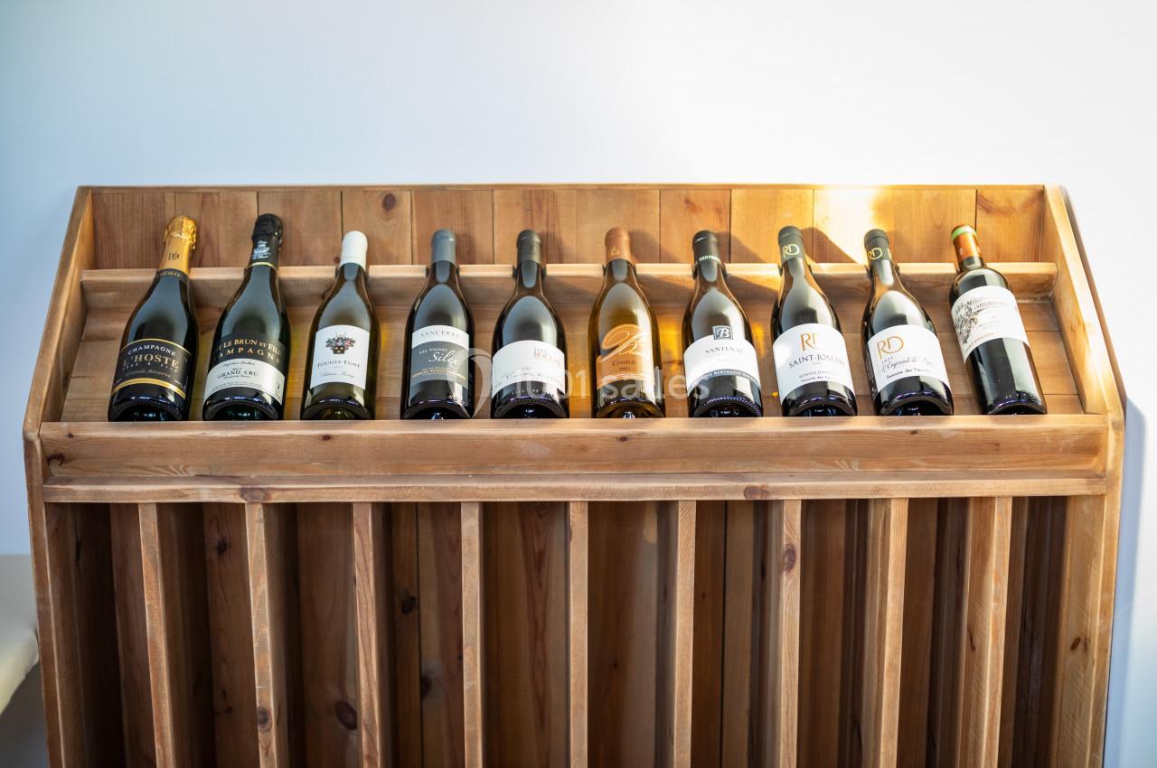 Bouteilles de vin alignées sur un présentoir en bois, éclairées par une lumière naturelle.