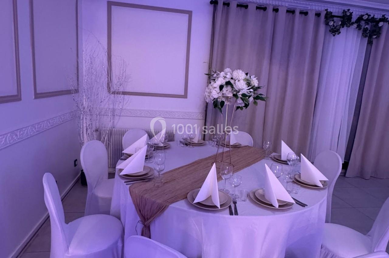 Table ronde élégamment dressée avec nappes blanches, serviettes pliées, vaisselle et centre de table floral dans une salle…