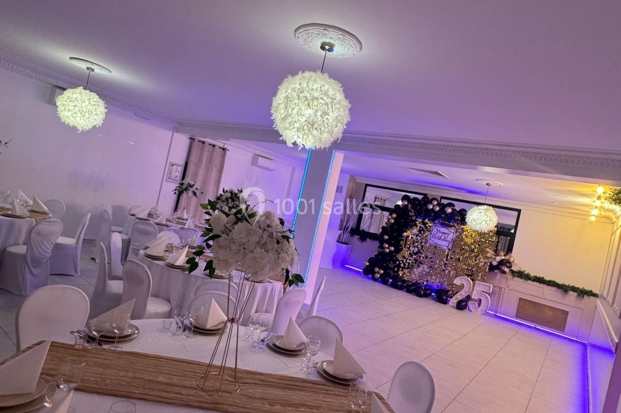 Salle de réception décorée avec des tables dressées, des chaises blanches et un espace lumineux avec éclairage violet.