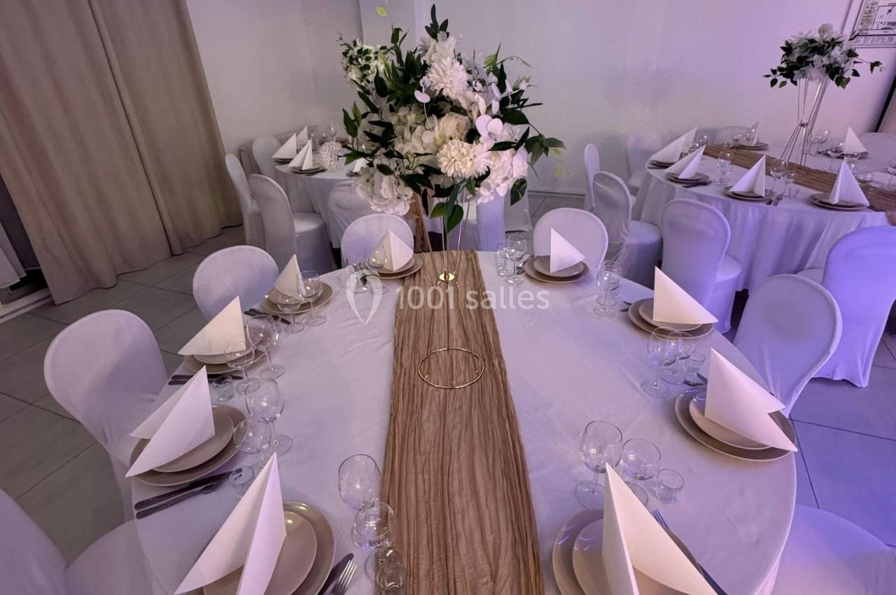 Table ronde décorée pour un événement, avec nappes blanches, serviettes pliées, vaisselle élégante et centre floral.
