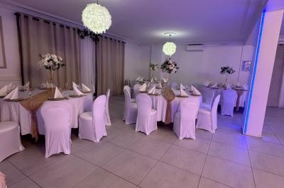 Enseigne lumineuse ’Baron’ entourée de verdure, avec des roses au premier plan et une façade éclairée en arrière-plan.