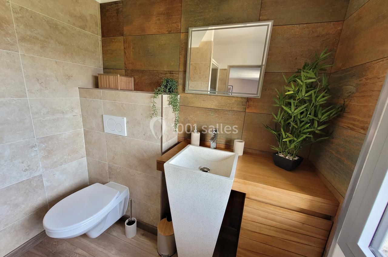 Salle de bain moderne avec toilettes suspendues, lavabo design, meuble en bois et plantes décoratives.
