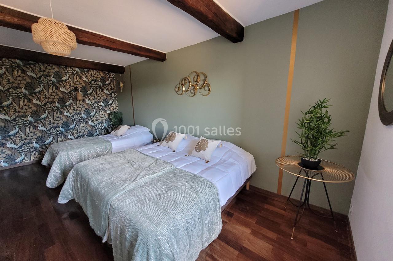 Chambre avec deux lits doubles, parquet, mur vert orné, papier peint floral et décoration végétale.