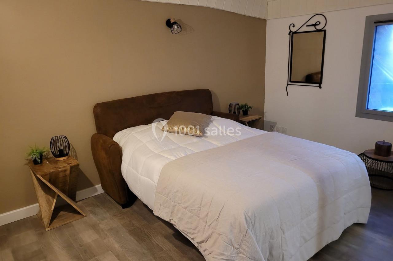 Lit double avec couverture blanche dans une chambre au mur beige, décorée de tables de chevet et d'un miroir mural.