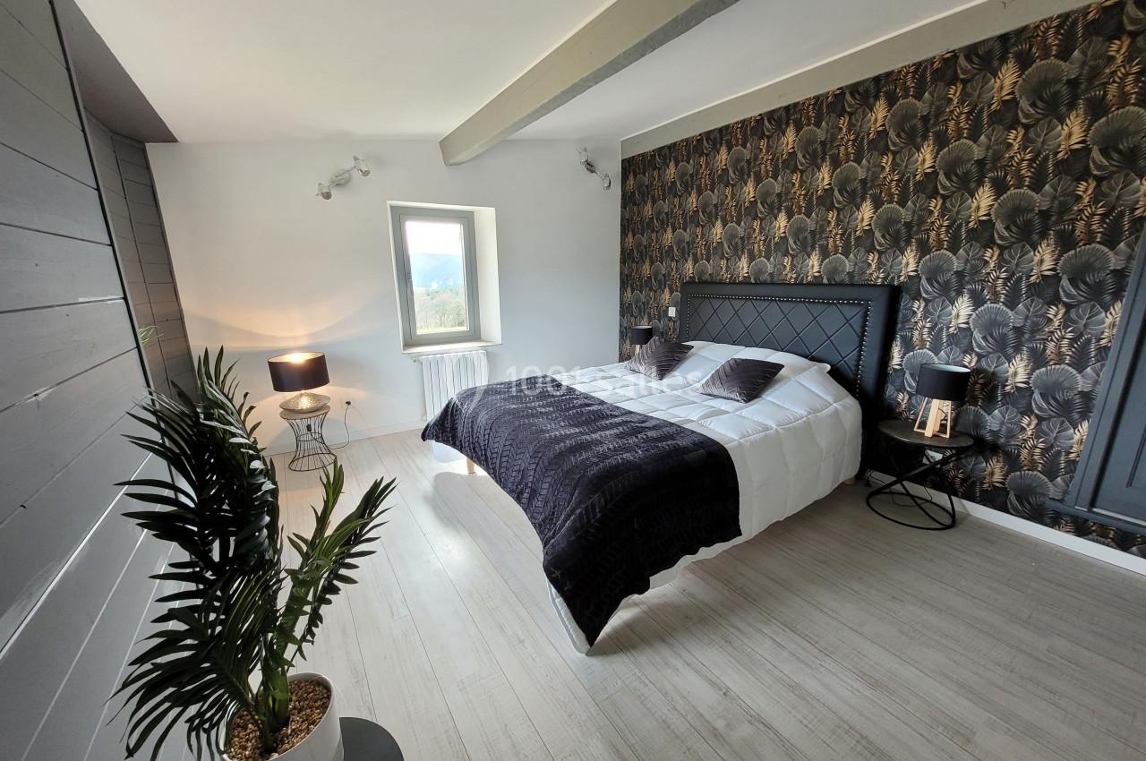 Chambre lumineuse avec lit double, mur décoré de papier peint floral sombre, lampe et plante en pot.