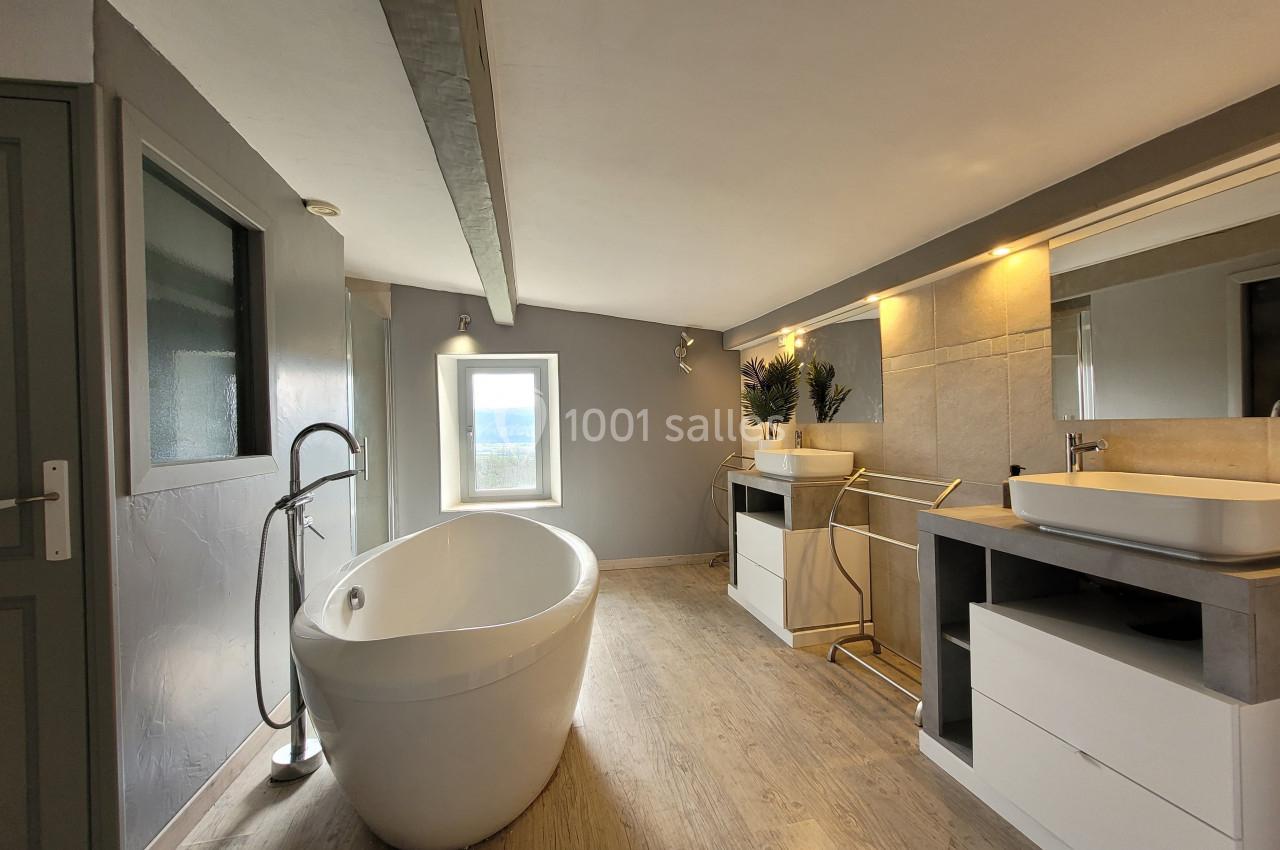 Salle de bain moderne avec baignoire îlot, vasques blanches, meubles intégrés et lumière naturelle.