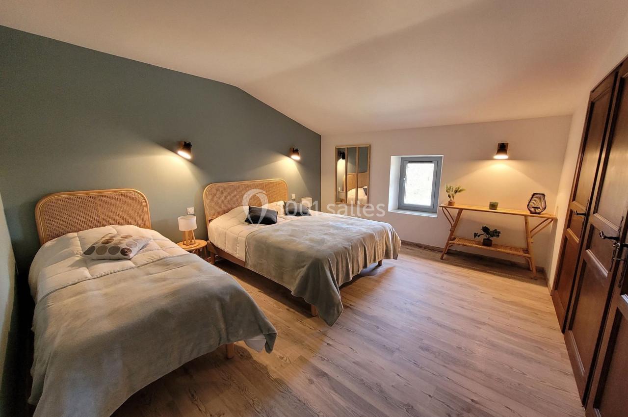 Chambre lumineuse avec deux lits simples, murs verts et blancs, parquet clair, table en bois et fenêtre.