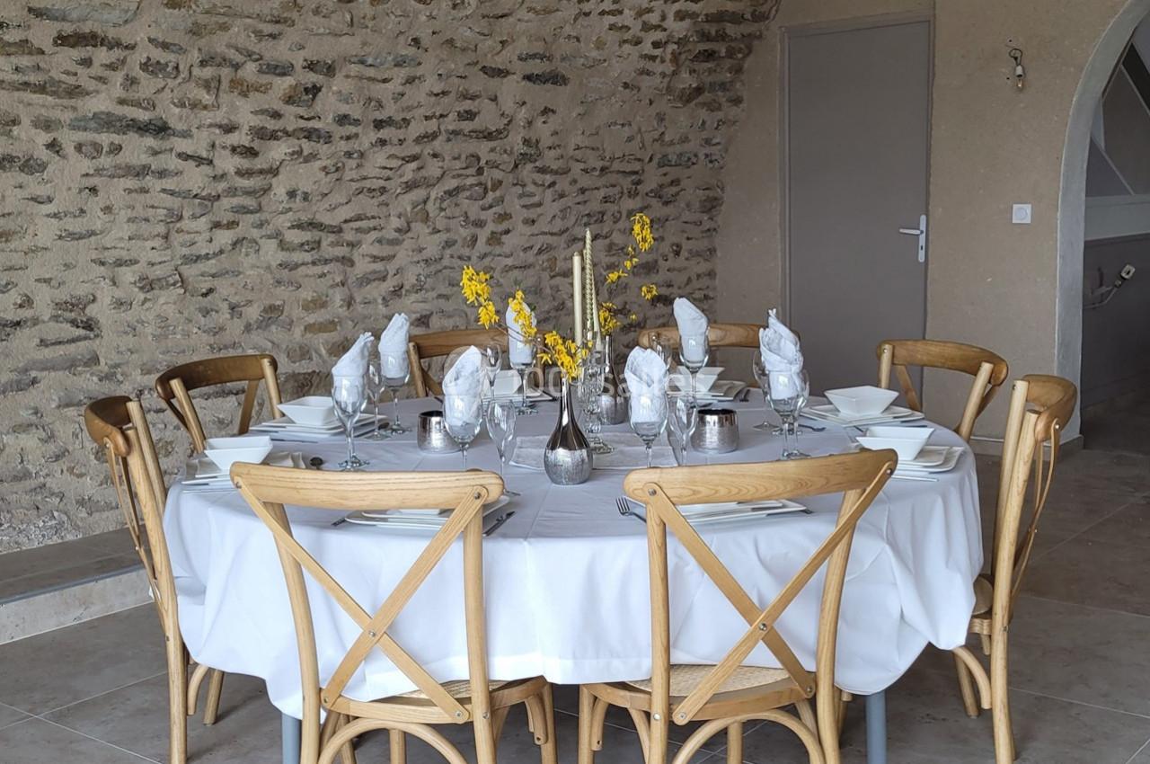 Table ronde dressée avec une nappe blanche, vaisselle élégante, serviettes pliées et décoration florale jaune.