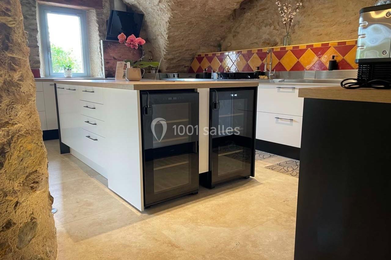 Cuisine rustique avec murs en pierre, îlot central moderne, carreaux colorés et électroménagers intégrés.