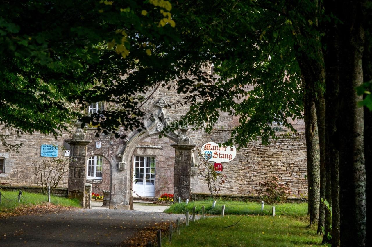 Entrée d'un bâtiment en pierre entouré d'arbres, avec une arche et des panneaux visibles près de l'entrée.