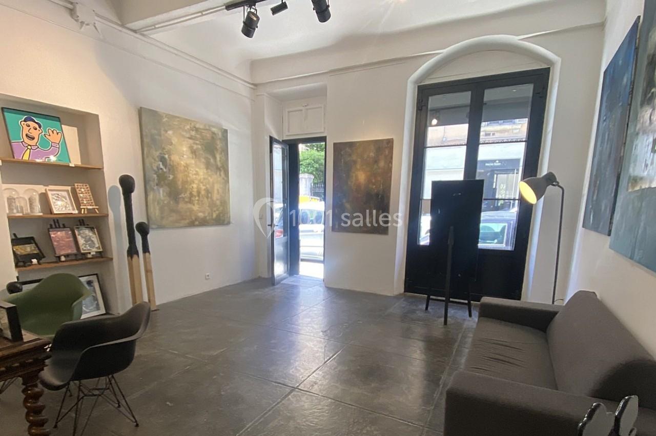 Galerie d'art lumineuse avec des peintures accrochées aux murs, mobilier minimaliste et grande porte-fenêtre.