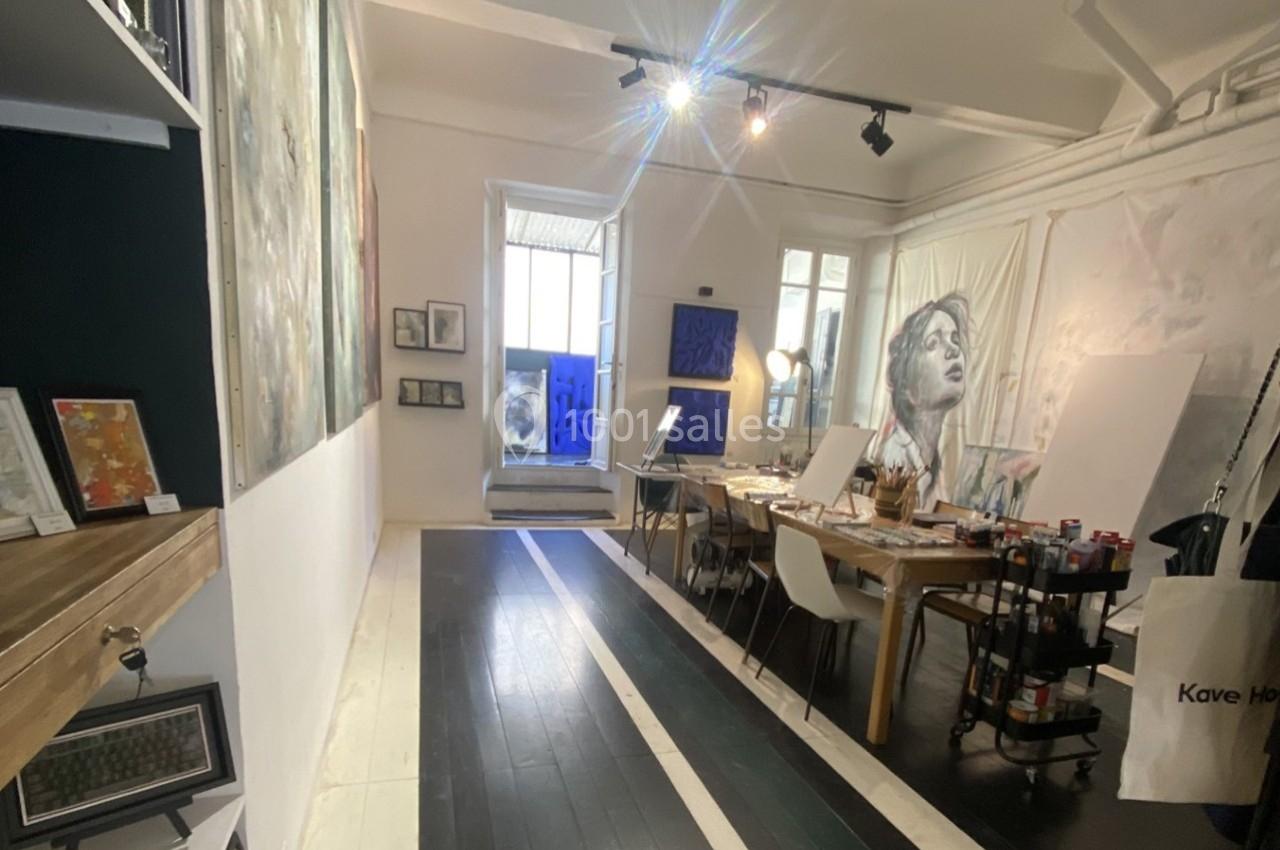 Atelier d'art lumineux avec des peintures exposées, des tables de travail et des fournitures artistiques.