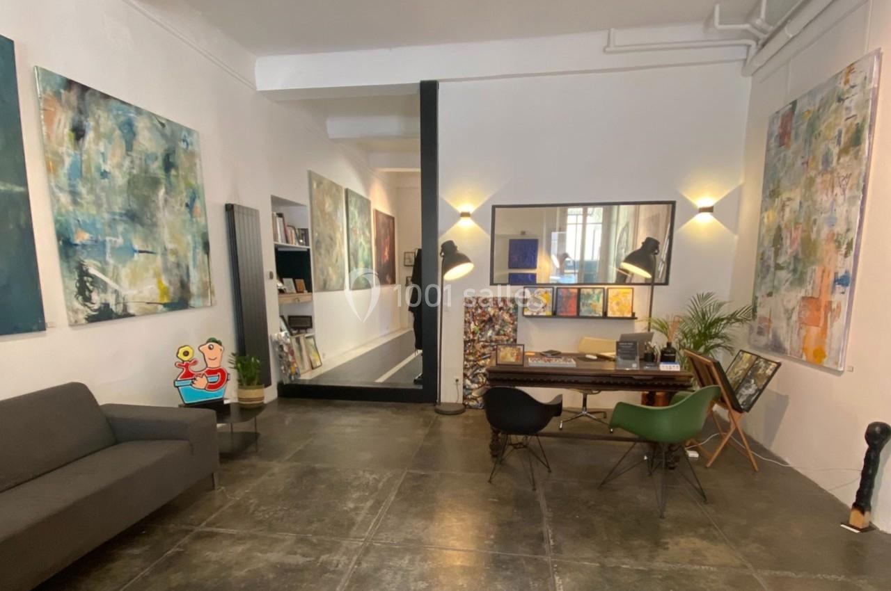 Intérieur d'une galerie d'art avec des peintures abstraites accrochées aux murs et un espace de travail aménagé.